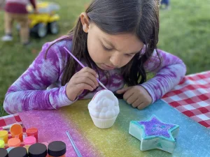 Little girl painting a ceramic ice cream cone. Crafting on a picnic table.